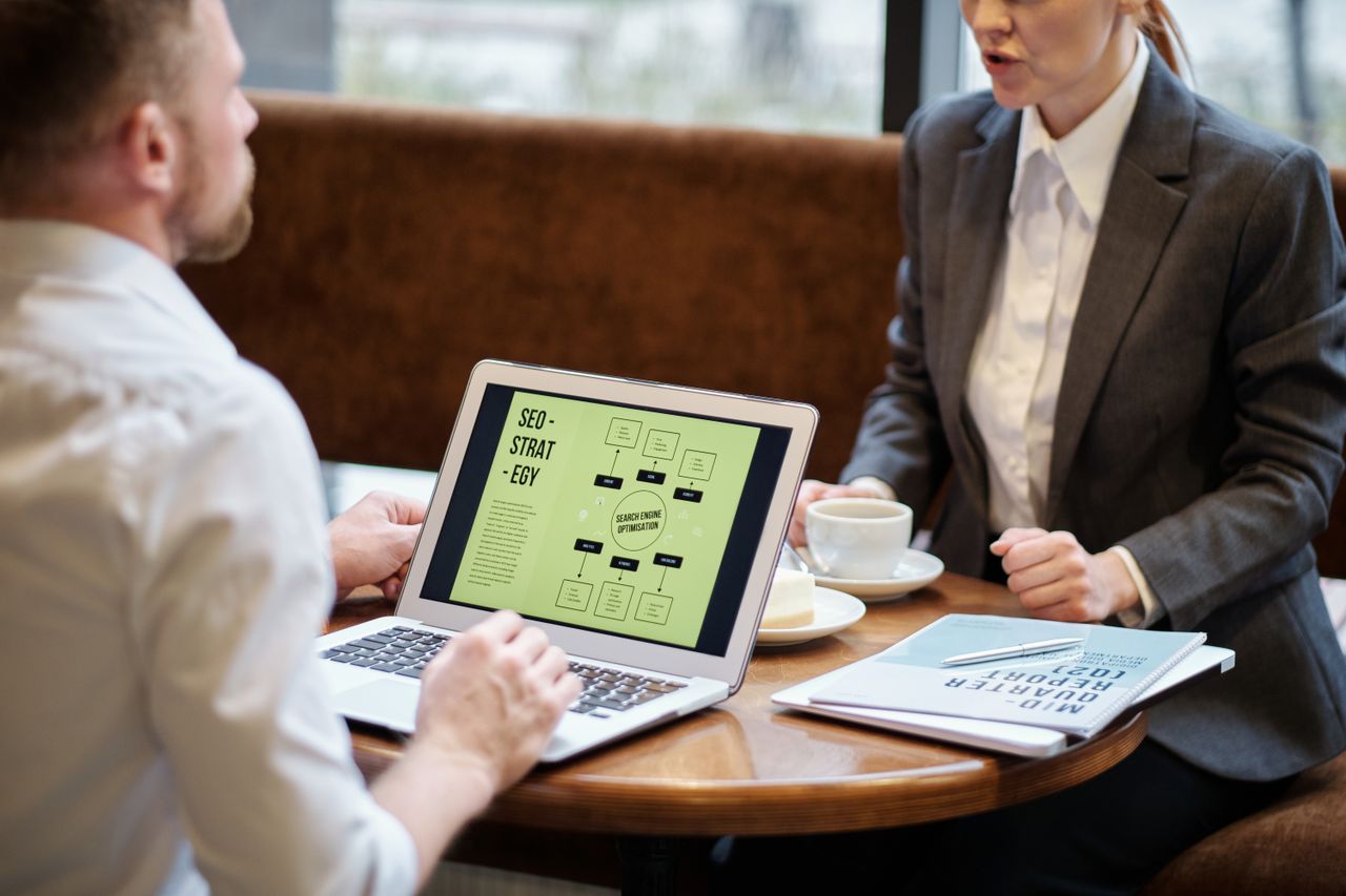 services-03 A man and woman engaged in a business meeting discussing SEO strategy in a cozy cafe setting.
